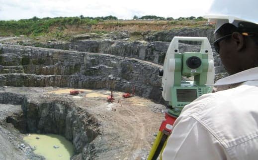 Surveyor with a total station overlooking a quarry site